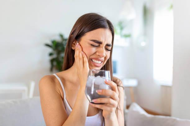 a woman with a toothache holding a glass of water with lots of ice