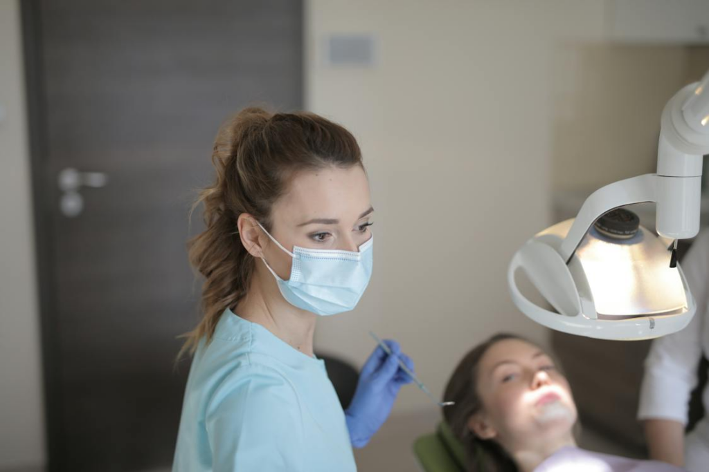 a dental professional wearing a mask looking at something with the patient laying on the dentist chair
