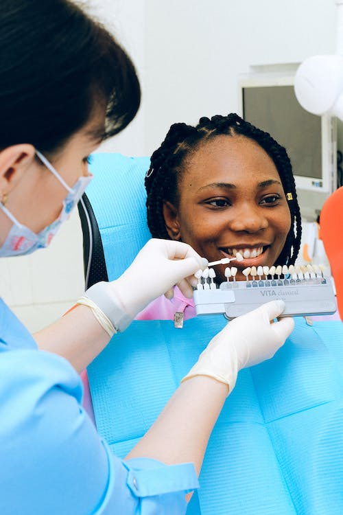 a dental professional holding a palette of dental crown in front of a patient 