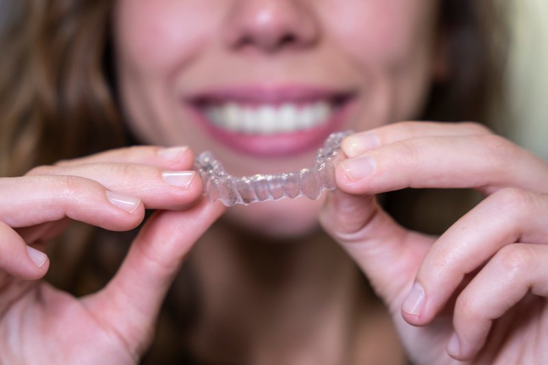 Smiling woman holding out Invisalign aligner