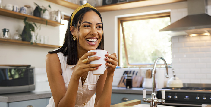 Woman smiling while drinking coffee in kitchen