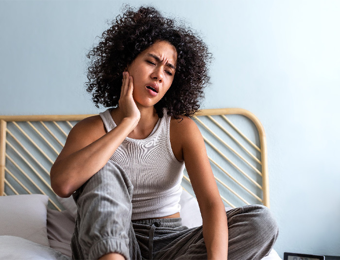 Woman sitting on bed with tooth pain.